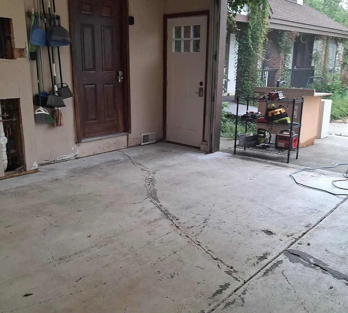 An untreated residential garage slab with a long crack running diagonally across it and dark staining along the joints.