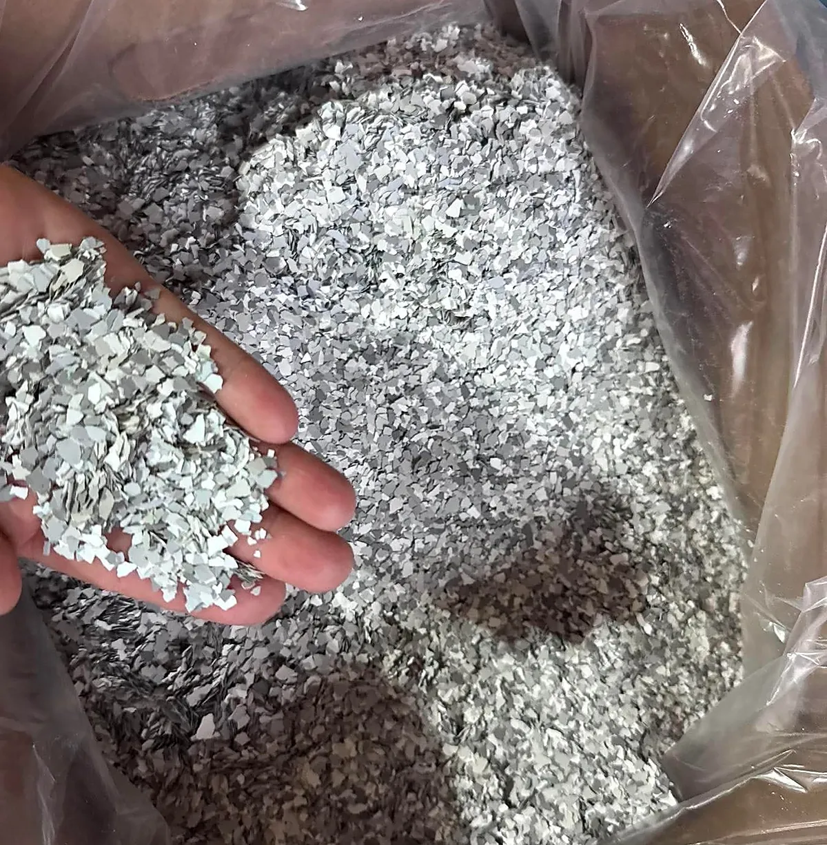 A hand lifting a palmful of grey, white and black vinyl flake chip out of an open bag of the blend.