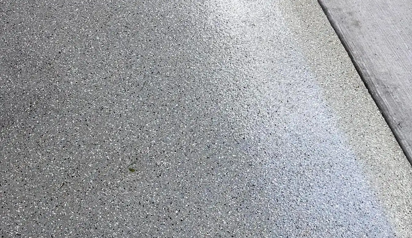 Close-up of a cured grey, white and black flake epoxy surface meeting a strip of plain untreated concrete along a straight edge.