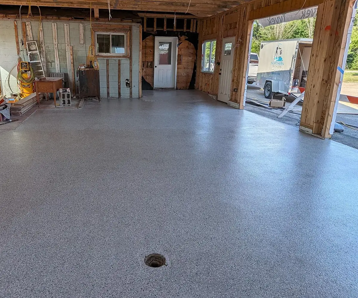 A finished grey flake epoxy floor filling a garage bay, with the open door looking out onto an enclosed work trailer parked outside.