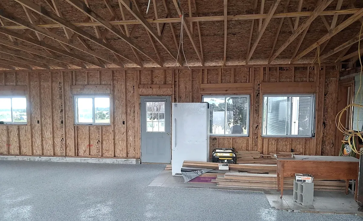 Completed flake epoxy floor across a pole barn being set up as a workshop, with a timber workbench and stacked lumber along the far wall.