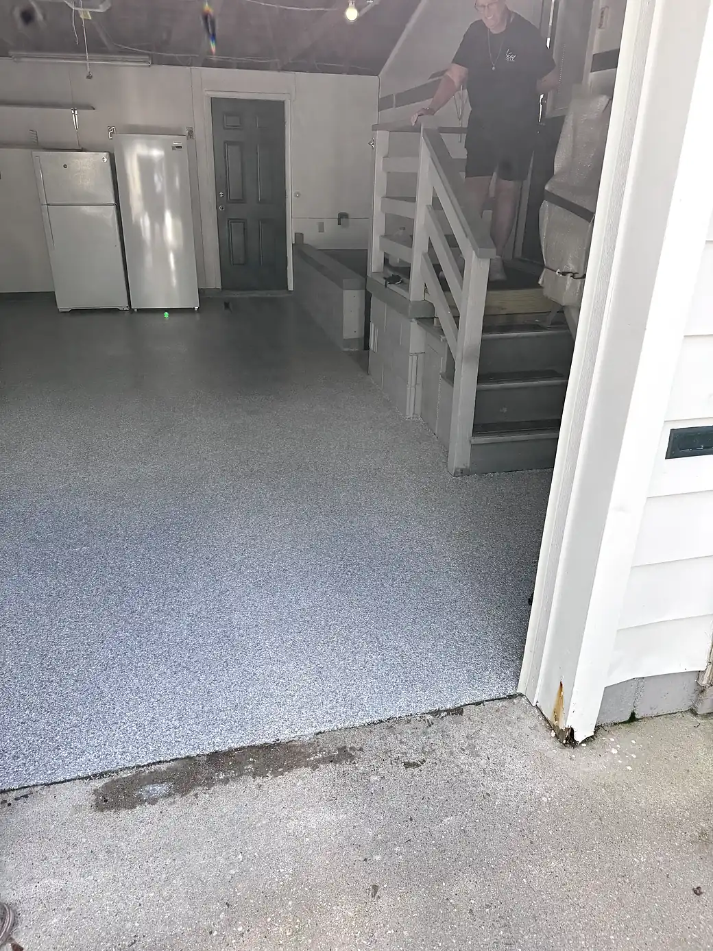 The coated floor seen from the garage doorway, stopping in a clean line where it meets the bare concrete apron outside.