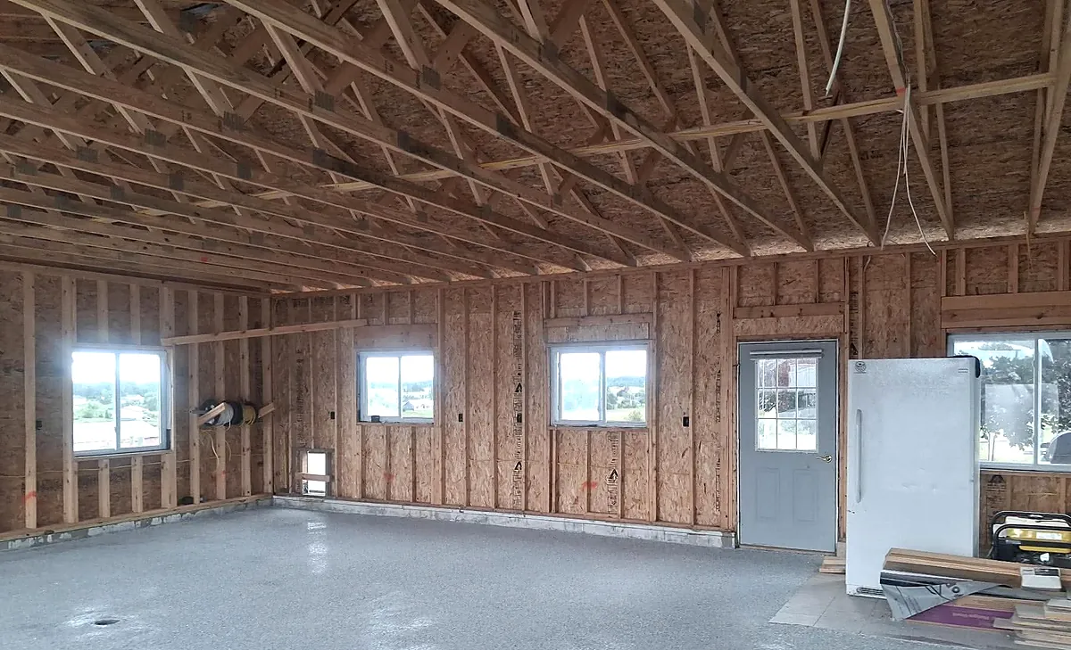 Wide view of a completed flake epoxy floor beneath open roof trusses in a newly framed pole barn.